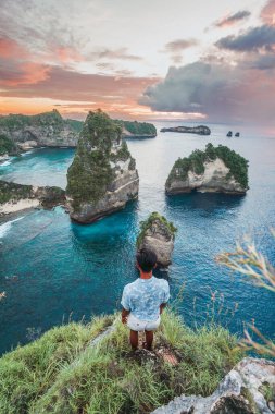 Rock Hill 'deki adam okyanusta gün batımını seyrediyor Nusa Penida, Bali, Endonezya' da