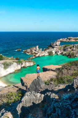 Uçurumun kenarında duran ve mavi okyanusa bakan bir adam. yaz arkaplanı ve yaz tatili kavramı
