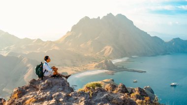 Endonezya 'daki Komodo Ulusal Parkı' ndaki Padar Adası 'nın güzel manzarasına bakan bir uçurumda oturan genç bir adam. Yaz ve yaz tatili