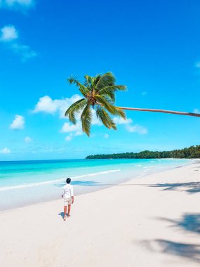 Tropik plajda palmiye ağaçlarıyla beyaz elbiseli güzel Asyalı kadın.