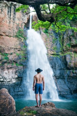 Bir adam ormandaki bir şelalenin güzelliğine hayran.