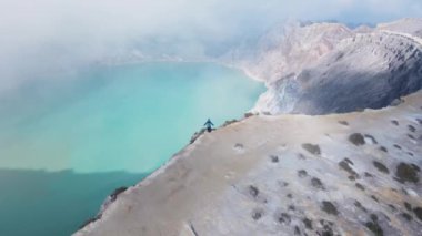 Bir adam, Endonezya 'nın Doğu Java kentindeki Kawah Ijen volkanında turkuaz sülfür gölü bulunan kayalık bir volkanın kenarındaki manzaraya hayran kalır.