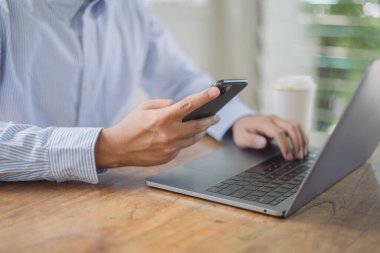 Cep telefonu kullanan, internette gezen ve bilgisayarla çalışan bir adam.