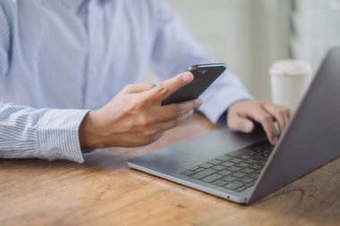 Ofis masasında dizüstü bilgisayarla çalışan bir iş adamı. Çevrimiçi olurken elinde cep telefonu tutan bir adam ev ofisinden dizüstü bilgisayarla çalışıyor.