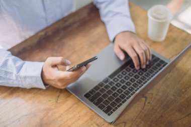 Evden çalışıyorum. İnternette cep telefonu kullanan sıradan bir iş adamı ev ofisinden laptop bilgisayarı üzerinde çalışıyor.