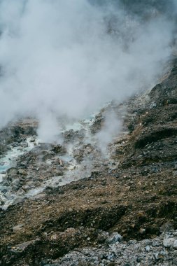 Nehir, duman püskürten bir volkanın kayalık tabanı boyunca akar.