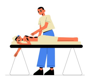 Erkek masaj terapisti masaj masasında yatan bir kadına sıcak taş terapisi seansı sunuyor. Sahne, rahatlama ve refah üzerine odaklanmış profesyonel bir spa tedavisini temsil ediyor.