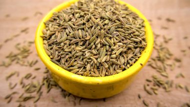 Fennel Seeds Isolated Closeup in a Bright Yellow Bowl on Wooden Surface clipart