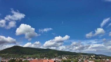 Açık mavi bir gökyüzü, birkaç bulut ve arka planda bir dağ. Gökyüzü sakin ve huzurlu, ve bulutlar sahneye derinlik katıyor.