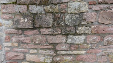 Yüzeyde pembe, gri ve krem tonlarında doğal taşlardan oluşan taştan bir duvar sergileniyor. Her taş eşsiz doku ve desenler sergiliyor, yaşlanma ve yıpranma hikayesi anlatıyor. Ara sıra yosun yosunları ekleyin.