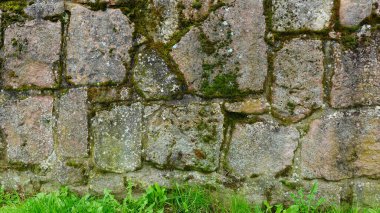 This view showcases an ancient stone wall, characterized by its weathered and irregularly shaped stones, some of which are covered in vibrant green moss. The wall reflects a rich history, suggesting clipart