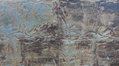 Dokulu bir duvar yüzeyinin detaylı bir görüntüsü sessiz mavi ve kahverengi tonlarda karmaşık desenleri ortaya çıkarır. Yüzeyde doğal yaşlanma ve sanatsal tasarım karışımı sergileniyor. Renklerin ve dokuların karışımı organik ve katmanlı bir görünüm yaratıyor.