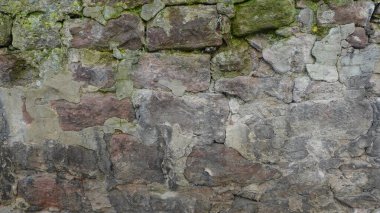 Antik taş duvar jeoloji ve tarihin bir karışımını sergiliyor. Zamanın eşsiz dokuları sayesinde zamanın katmanlarını ortaya çıkarıyor. Yıpranmış taşlar, dilsiz grilerden ince kahverengilere kadar çeşitli tonlar sergiliyor ve çağın işçiliğini vurguluyor. Yosun ve zambak