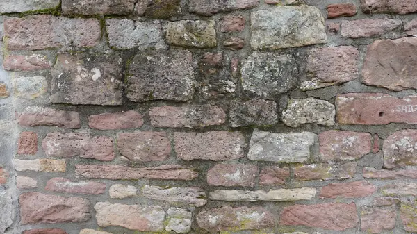 Yüzeyde pembe, gri ve krem tonlarında doğal taşlardan oluşan taştan bir duvar sergileniyor. Her taş eşsiz doku ve kalıplar sergiliyor, bir yaş ve yaş hikayesi anlatıyor.