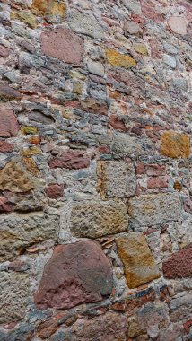 Antik bir taş duvarın yüzeyi, gri, kahverengi ve soluk pembenin tonlarını içeren renk ve renklerin bir karışımını gösteren zengin bir duvar halısını ortaya çıkarır. Her taşın şekli ve boyutu benzersizdir.