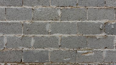 Kaba dokulu gri beton blok bir duvar belirgin bir şehir ortamında duruyor ve sağlam inşaat malzemelerini sergiliyor. Bloklar tipik bir şablona göre dizilmiş. Duvarcılık izleri var. Bazı bölümlerde düzensiz surfa vurgulanıyor