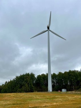 Vertical photo of a wind turbine in an agricultural field with haystacks against a cloudy sky. Space for text. Perfect for themes of alternative energy, environmental issues, and resource scarcity. clipart