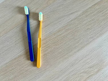 Açık ahşap bir yüzeyde mavi ve sarı diş fırçalarının minimalist fotoğrafı. Diş bakımı için ideal, ağız temizliği promosyonları, veya yazı için yeri olan tasarımlar, temizliği ve sağlıklı alışkanlıkları vurgulamak için