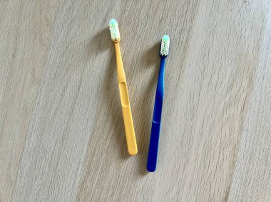 Açık ahşap bir yüzeyde mavi ve sarı diş fırçalarının minimalist fotoğrafı. Diş bakımı için ideal, ağız temizliği promosyonları, veya yazı için yeri olan tasarımlar, temizliği ve sağlıklı alışkanlıkları vurgulamak için