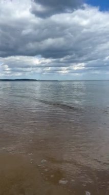 Baltık Denizi 'nin kumlu sahilde dalgalar halinde yuvarlanışını gösteren dikey bir video. Sakin deniz, sahil, doğa, okyanus, sükunet, deniz kenarı, rahatlama, sahil manzarası, huzurlu dalgalar..