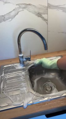 Metal mutfak lavabosunu süngerle yıkayan kauçuk eldivenli bir kadının dikey videosu. Temizlik, temizlik, ev işleri, mutfak, ev işleri, ev işleri, lavabo temizliği, ev bakımı..