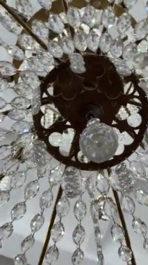Tavandan sarkan büyük bir kristal avizenin dikey videosu. Parlak ışıklar ve karmaşık detaylarla parlıyor. Lüks iç mekan, klasik dekor, zarafet, zenginlik, büyük aydınlatma armatürü..