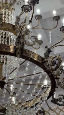 Tavandan sarkan büyük bir kristal avizenin dikey videosu. Parlak ışıklar ve karmaşık detaylarla parlıyor. Lüks iç mekan, klasik dekor, zarafet, zenginlik, büyük aydınlatma armatürü..