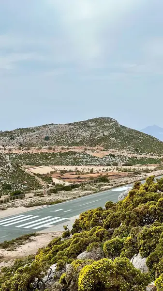 Dikey fotoğraf. Yunanistan 'ın Kastellorizo Adası' ndaki tepeler arasında küçük bir havaalanı pisti uzanıyor. Uzak ada seyahati, Yunan manzarası, havacılık, ulaşım, Akdeniz manzarası, yaz turizmi. 