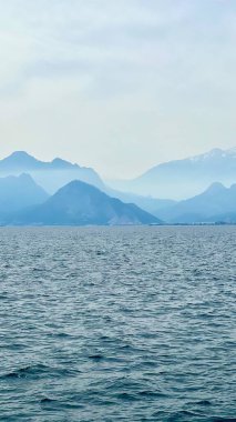 Sakin denizin üzerindeki dağ siluetinin dikey fotoğrafı. Parlayan suyla birlikte. Akdeniz, yaz tatili, seyahat, kıyı manzarası, huzurlu manzara, Antalya, Türkiye, sakin doğa manzarası. 