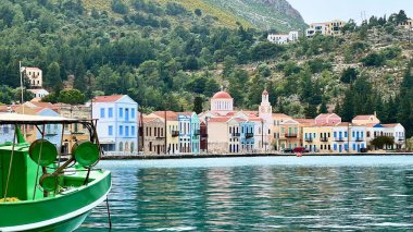 Kastellorizo, Yunanistan, 28 Mar 2025: Açık gökyüzü altında tekneleri olan renkli evler ve küçük bir liman. Akdeniz ada manzarası, huzurlu kasaba, deniz kıyısı atmosferi, bahar seyahatleri.. 