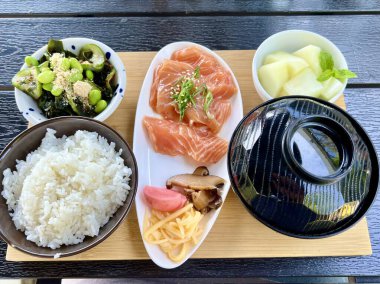 Geleneksel Japon öğle yemeği seti koyu ahşap masada taze sashimi, pilav, miso çorbası, turşu sebze, yosun salatası ve kavun. Asya mutfağı, sağlıklı beslenme, restoran, otantik yemek..