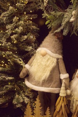 Süslerle süslenmiş bir Noel ağacının yanında duran tüylü beyaz sakallı, sivri şapkalı ve süpürgeli, neşeli bir cüce süsü.