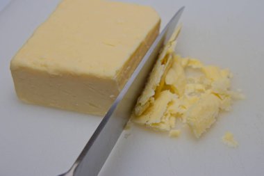 Bir bıçak bir peynir bloğunu kesiyor, bazı parçaların parçalanmasına neden oluyor. Görüntü, çizgili bandın dokusunu ve bıçağın keskinliğini vurguluyor. Bu, yemek hazırlama tekniklerini göstermek için geçerlidir..