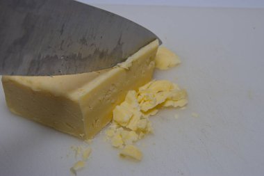 Bir bıçak bir peynir bloğunu kesiyor, bazı parçaların parçalanmasına neden oluyor. Görüntü, çizgili bandın dokusunu ve bıçağın keskinliğini vurguluyor. Bu, yemek hazırlama tekniklerini göstermek için geçerlidir..