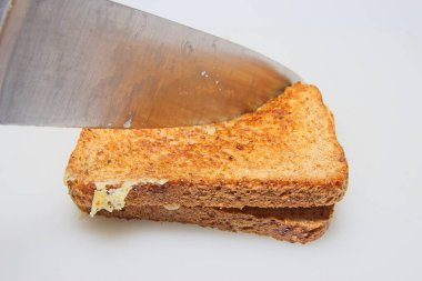 Bir bıçak kızarmış peynirli sandviçi iki dilim kızarmış ekmek ve aralarında erimiş peynir ile keser. Resim dilimleme anını yakalar ve ekmeğin dokusunu ve erimiş peyniri gösterir..