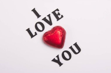 Kırmızı Çikolata 'nın kalbini kullanarak beyaz arka planda siyah tahta harfleri temsil ediyorum., 