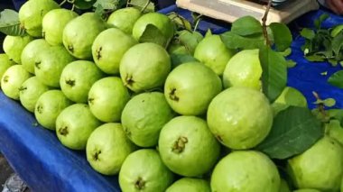 Açık hava pazarında satılık mavi bir tepside sergilenen canlı yeşil guava yığını.