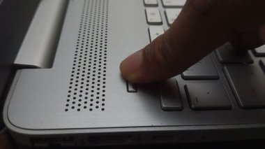 Bir parmak gümüş dizüstü bilgisayarın güç düğmesine basar. Dizüstü bilgisayarlar klavye ve hoparlör ızgarası görünür durumda. Eylem, aygıtın başlatılmasını veya kapatılmasını gerektirir.