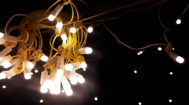 Sarı kabloyla sarılı bir sicim lambası kümesine yakın çekim, koyu bir arkaplan üzerine sıcak bir parıltı yayıyor. Birçok ampul sahneyi aydınlatır.
