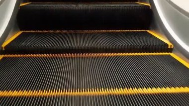 Yürüyen merdivenlerin yakın görüntüsü var. Sarı çizgili siyah adımlar, modern bir ortamda mekanizma tasarımı ve yukarı doğru hareketi sergiliyor..