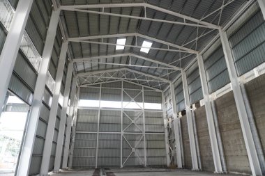 Industrial hangar with a metal frame. High steel columns and beams support the roof made of metal profiles. The interior walls are covered with metal panels. clipart