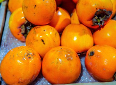 Hurmalar bir pazar rafında güzelce düzenlenir. Parlak, pürüzsüz, parlak ve turuncu. Mevsimsel ürünler, sağlıklı beslenme veya gıda perakendecisi ile ilgili konular için uygundur.