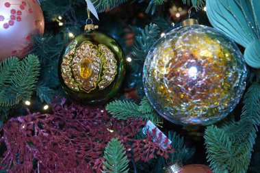 Noel ağacı şenliği. Ağaçta modern Noel süsleri asılı. Zarif cam toplar, pırıl pırıl yıldızlar ve altın, gümüş ve yumuşak pastel tonlarında karmaşık metal süsler..