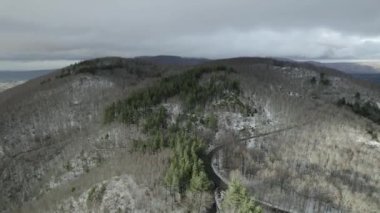 Bir dron, el değmemiş beyaz yamaçların üzerinde, sisli bulutlar arasında süzülür. İnsansız hava aracının hava görüntüsü çarpıcı bir dağ yolunu yakalıyor. Karla kaplı dramatik bir arazide dönüyor..