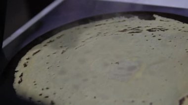 Elektrikli gözleme makinesi. Krep hamuru sıcak yüzeye dökülüyor, sonra da ince, yuvarlak bir katmana eşit bir şekilde gözleme spatulası ile yayılıyor. Hamur çabuk pişiyor, altın gibi yumuşak bir krep yapıyor..