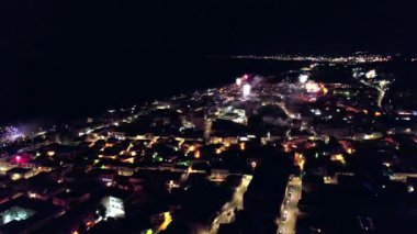 Küçük bir kasabada insansız hava aracı tarafından yakalanan muhteşem yeni yıl havai fişek gösterisi. Parlayan renkli ışıklar gece gökyüzünü aydınlatıyor, yakınlardaki binalardan yansıtıyor ve büyülü bir atmosfer yaratıyor..
