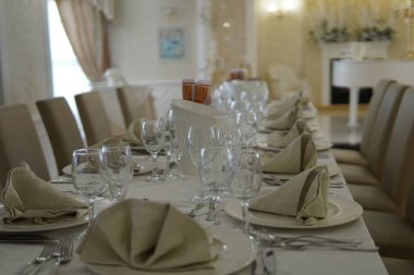 Resmi bir ziyafette zarif bir yemek masası. Masa krem masa örtüleriyle süslenmiş, sandalyeler döşenmiş. Arka planda beyaz bir piyano ve altın dekoratif elementler var..