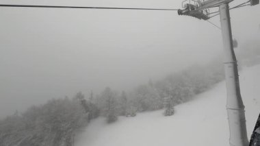 Bir kar fırtınası sırasında bir teleferik vadiden yükselir. Yoğun kar yağışı sırasında vadiden karlı bir dağa yükselen bir teleferiğin hava görüntüsü. Kış yolculuğu, turizm ve spor.