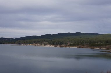 Sakin bir göl, aynaya benzeyen bir yüzey, uzak ormanın huzurlu kucaklamasının yansıttığı..