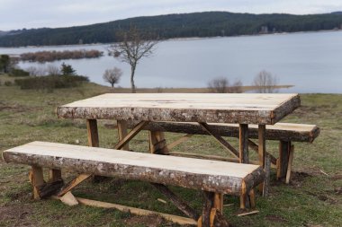 Göl kenarındaki tahta masa. Doğanın kalbinde yer alan kırsal ahşap masa sakin bir gölün sakin sularının üzerinde zarif bir şekilde yükselir..